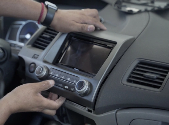 Close-up of a person installing or removing a car stereo unit and climate control panel from the dashboard of a vehicle.