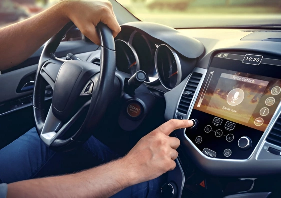 Driver using the voice control feature on a modern car infotainment system, with their hand on the touchscreen and the other on the steering wheel.