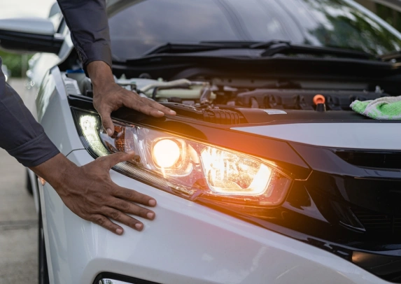 Person adjusting the headlight of a white car with the hood open, while the lights are turned on.