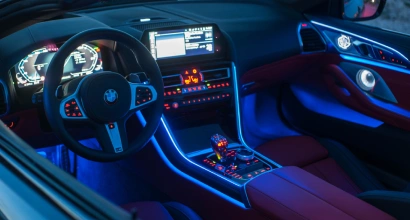 Interior of a BMW featuring ambient blue LED lighting across the dashboard, center console, and doors, highlighting modern digital displays and red leather seats.