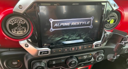 Close-up of a Jeep dashboard featuring an Alpine Restyle touchscreen display with rugged-themed graphics, surrounded by custom air vent covers reading "Tequila Patrol 4x4" and "Tactical Nachos."