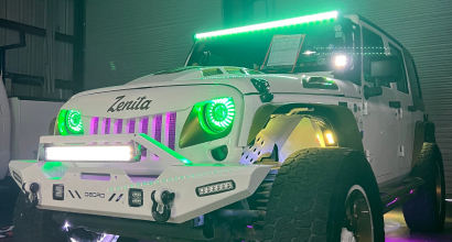 Custom white Jeep Wrangler with green LED halo headlights, a green LED light bar, and multiple auxiliary lights, showcased indoors under accent lighting.