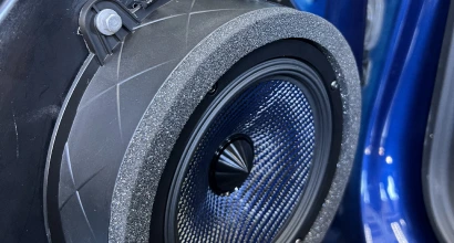 Close-up of a high-performance car speaker installed in a door panel, surrounded by a foam ring for acoustic isolation and mounted in a blue vehicle.