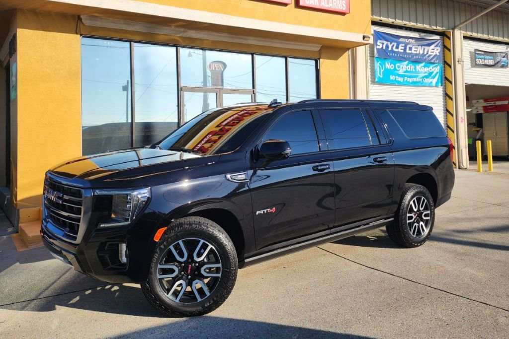A black GMC SUV with dark-tinted windows is parked outside Extreme Car Audio on a sunny day, showcasing a clean, professional tint job that enhances the vehicle’s sleek look.