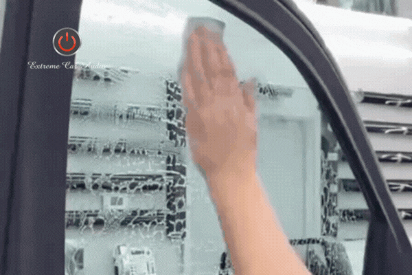 A close-up animation of a technician’s hand pressing and smoothing a window tint film onto a soapy vehicle window, with the Extreme Car Audio logo in the corner.