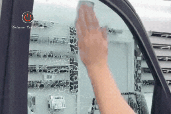 A technician wipes down a soapy car window in preparation for tint application, using smooth, even strokes. The Extreme Car Audio logo appears in the top corner, emphasizing professional service quality.