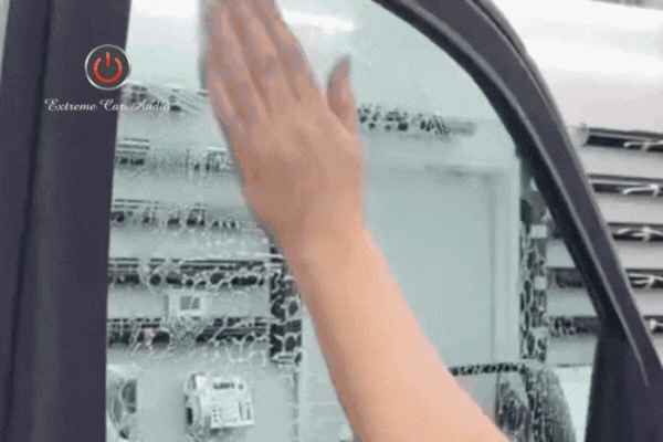 Close-up GIF showing a technician’s hand pressing and smoothing ceramic window film onto a car door window. The Extreme Car Audio logo appears in the corner as the tint film is applied over a layer of water and bubbles.