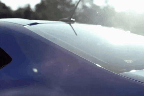 A close-up of a car's rear windshield gleaming in the sun as the camera pans across it, highlighting how window tint reflects sunlight. The bright glare and reflection emphasize the need for heat rejection in hot climates.