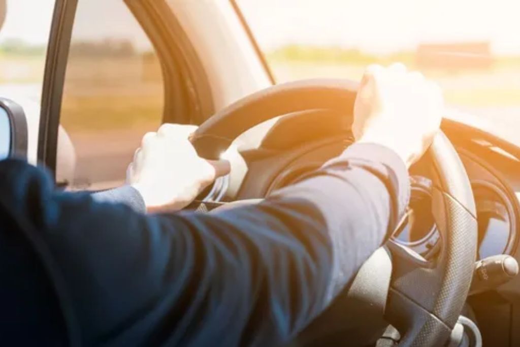 Sunlight pours through a car window as a driver grips the steering wheel, illustrating unprotected UV exposure during daily commutes. The bright glare emphasizes why window film is the unsung hero of skin care, offering continuous UVA and UVB protection inside vehicles.